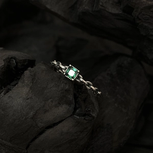 Vue macro d'une bague chaîne en argent avec zircon vert sur fond de charbon noir