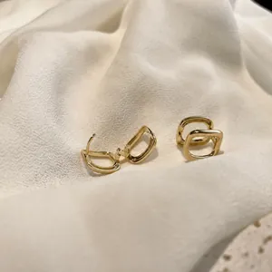 Minimalist geometric gold earrings with rounded square double-ring design on white silk