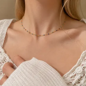 Collar dorado con cuentas de esmalte arcoíris en cadena fina sobre top de encaje blanco