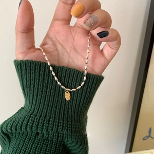 Collar minimalista de cuentas plateadas con colgante ovalado dorado sobre jersey verde