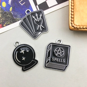 Three gothic enamel charms including magic crystal ball, sword heart, and spell book