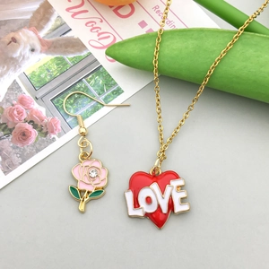 Detail of gold-tone alloy heart pendant with LOVE text and pink rose earring with crystals