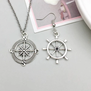 Vintage silver nautical compass necklace and ship wheel earrings set on a grey desk
