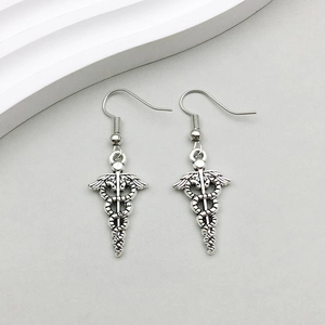 Detail view of antique silver medical Caduceus earrings on a clean gray background