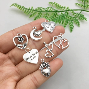 Close-up of seven vintage silver heart charms with intricate hollow floral and moon carvings