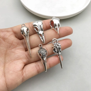 Five assorted antique silver bird skull pendants for DIY jewelry making held in hand
