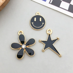 Close-up of black enamel alloy charms featuring a gold-rimmed smiley face, flower, and star