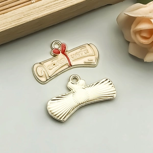 Detailed view of alloy graduate scroll charm with cream enamel and red bow detail