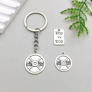 Vue macro des pendentifs d'haltères et plaque gravée YOU vs YOU sur le porte-clés sport