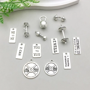 Gros plan de charms sportifs en argent antique avec haltères et disques de poids gravés