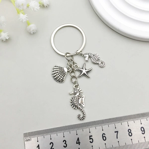 Detail of vintage silver seahorse starfish and shell keychain with a ruler for scale