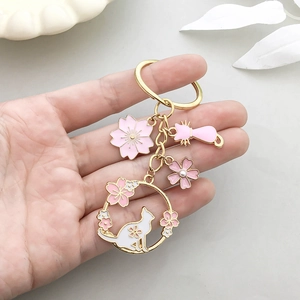 Porte-clés chat et fleur de cerisier rose avec anneau doré tenu par la main