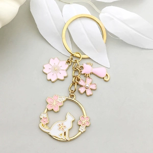 Détail de fleurs de cerisier et chat en émail rose sur un pendentif porte-clés doré