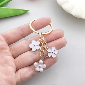 Porte-clés doré avec breloques fleurs en émail blanc tenu en main sur fond floral