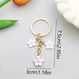 Porte-clés fleur dorée avec pétales en émail blanc et trois breloques long de 7,5cm