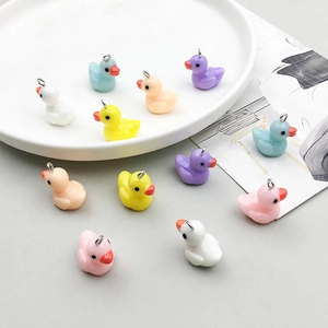 Colorful resin duck pendants with metal loops for DIY jewelry making on white ceramic plate