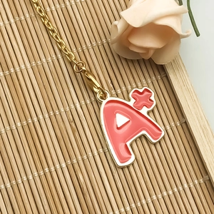 Close-up of pink enamel A+ letter pendant charm with lobster clasp on gold chain
