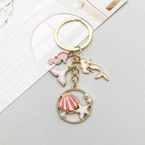 Detailed view of pink mermaid and seahorse alloy charms on a gold keychain with pearls