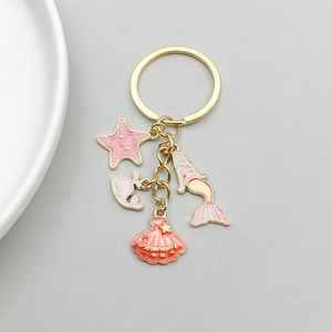 Détails des pendentifs sirène et étoile de mer en émail rose sur un porte-clés doré