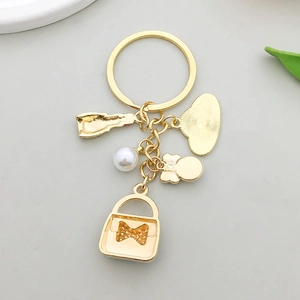 Détail d'un porte-clés doré avec charms de rouge à lèvres, perle et tête de dessin animé