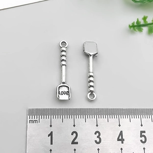 Detailed scale measurement of a silver shovel pendant with 'LOVE' engraving on grey base