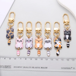 Set of 7 colorful enamel cat keychains with swinging tails shown with a measuring ruler
