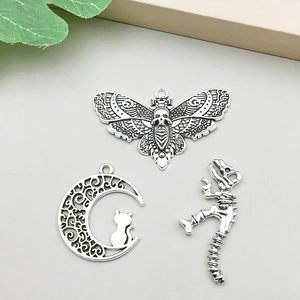 Detalle macro de dijes de plata antigua: polilla, gato en la luna y esqueleto para bisutería