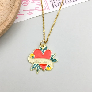 Close-up of golden necklace with heart-shaped BEST MAMA pendant and enamel carnation detail