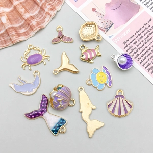 Detalle de dijes de conchas marinas de esmalte morado con acabado dorado y perlas