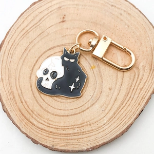 Detail of a black cat and white skull enamel pendant with golden lobster clasp and stars