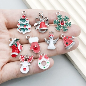 Mano che tiene ciondoli natalizi assortiti come albero, campana e cervo per gioielli DIY