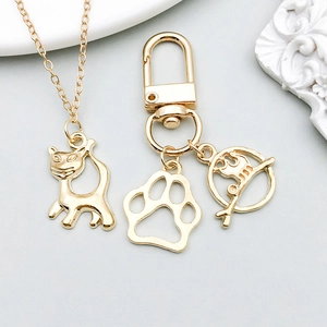 Detail of gold cat pendant necklace and paw keychain set on a minimalist background