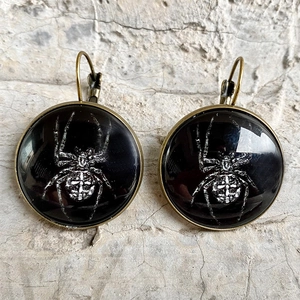 Detail view of gothic lever-back earrings featuring a white spider motif on glass cabochon