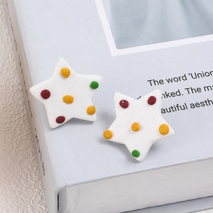 Minimalist white star earrings with colorful polka dots on a modern book background