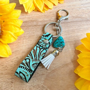 Détail de porte-clés en cuir vintage avec motif gaufré, turquoise et pompon blanc