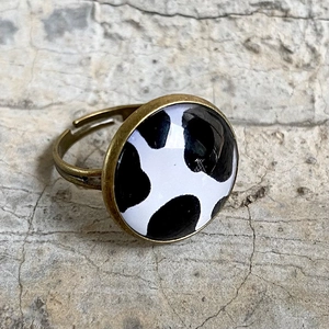 Makroaufnahme von Bronze-Ring mit Glas-Cabochon und schwarz-weißem Kuhmuster-Design