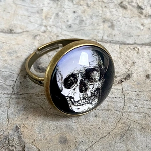 Detailansicht eines bronzenen verstellbaren Rings mit Totenkopfmotiv unter Glas