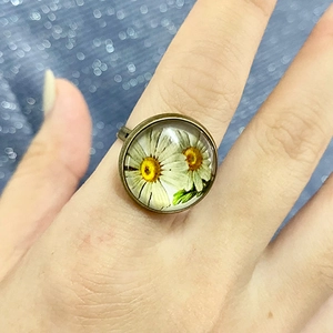Nahaufnahme eines Vintage-Bronze-Rings mit Glaskuppel und weißem Gänseblümchen-Muster