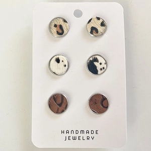 Detailed close-up of handmade round leather stud earrings featuring leopard and cow prints