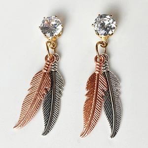 Dettaglio degli orecchini a piuma in stile western retrò con accenti bicolore oro rosa e argento