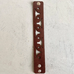 Détail du bracelet en cuir marron foncé avec motifs d'étoiles et de cornes évidés