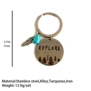 Macro shot of silver keychain with Explore engraving, feather charm and turquoise bead