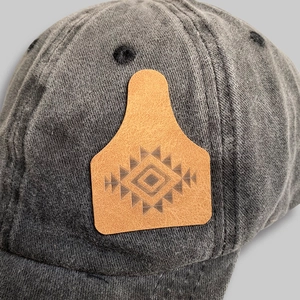 Macro detail of dark grey washed denim baseball cap with engraved brown leather patch