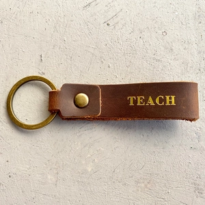 Close-up of brown crazy horse leather keychain with gold TEACH engraving for teachers