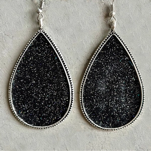 Détail de boucles d'oreilles argentées avec paillettes noires et bordure perlée