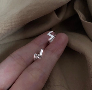 Détail macro de boucles d'oreilles éclair géométriques en argent S925 sur tissu brun