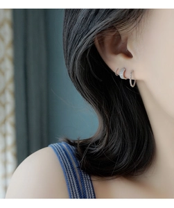 Vista macro de aros plateados trenzados con circonitas apilados en el lóbulo de oreja
