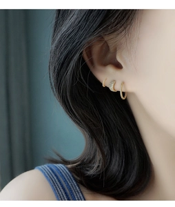 Vista detallada de tres pendientes de aro trenzados dorados y earcuff con circonitas