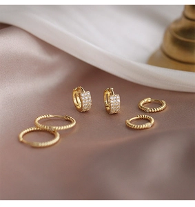 Detalle de pendientes de aro dorados y ear cuffs con circonitas sobre satén rosa