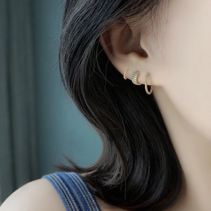 Set de tres pendientes de aro dorados trenzados y con circonitas lucidos por una modelo